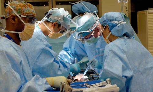 Five doctors working operating on a patient.
