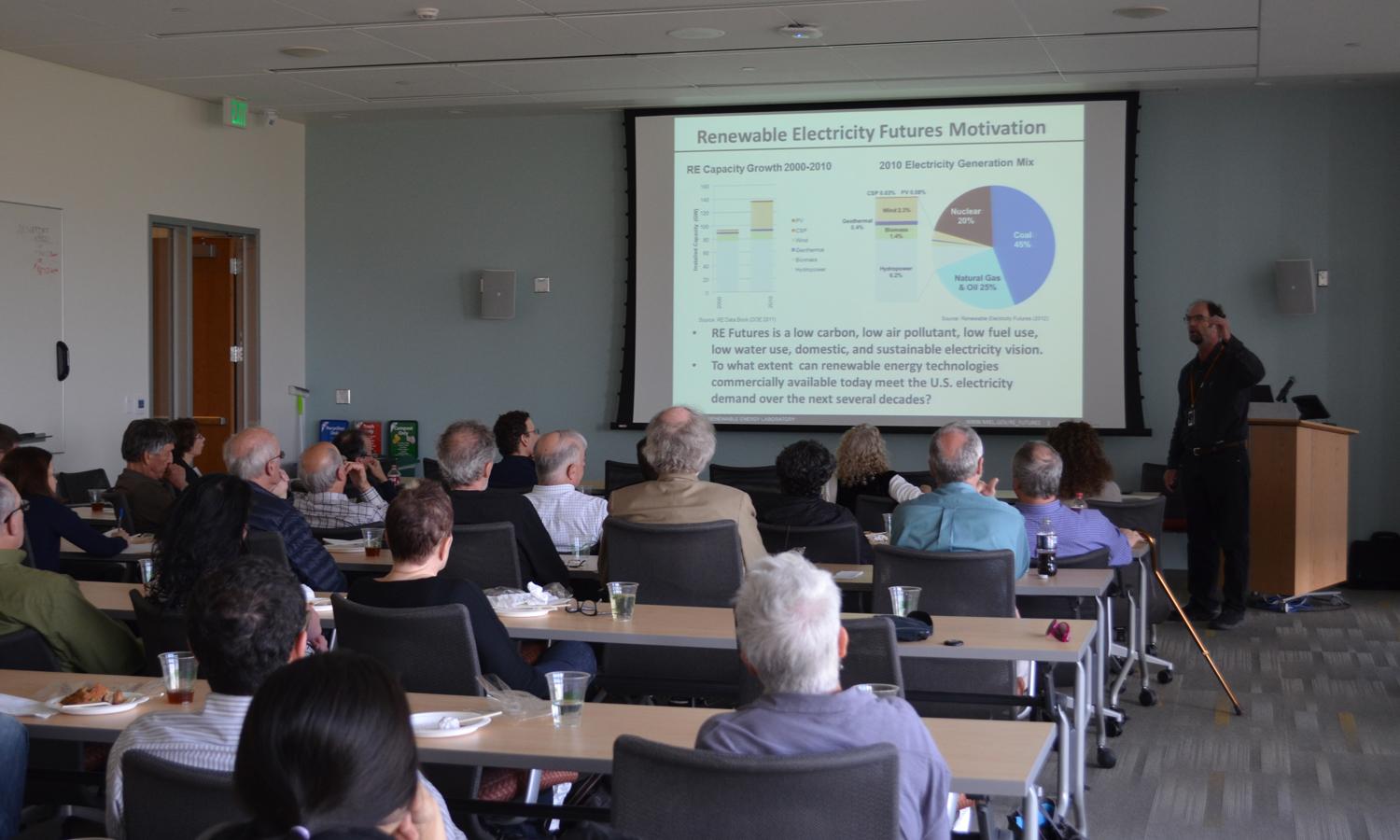 People sit in a room watching a presentation on renewable electricity. 